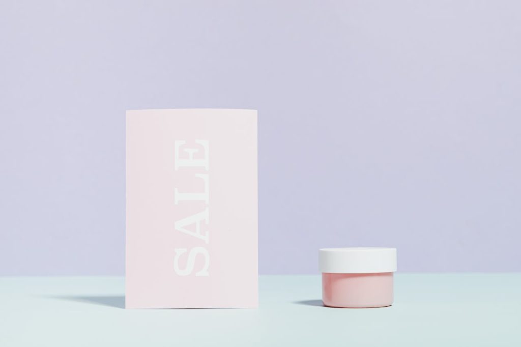Elegant still life of a sale card and cream jar on pastel background.
