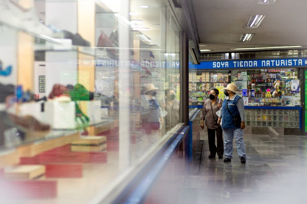 Adults wearing masks shop indoors at a marketplace, reflective display in view.