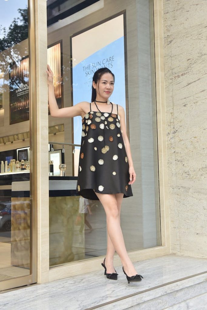 Stylish woman in a black floral dress poses confidently near a store entrance.
