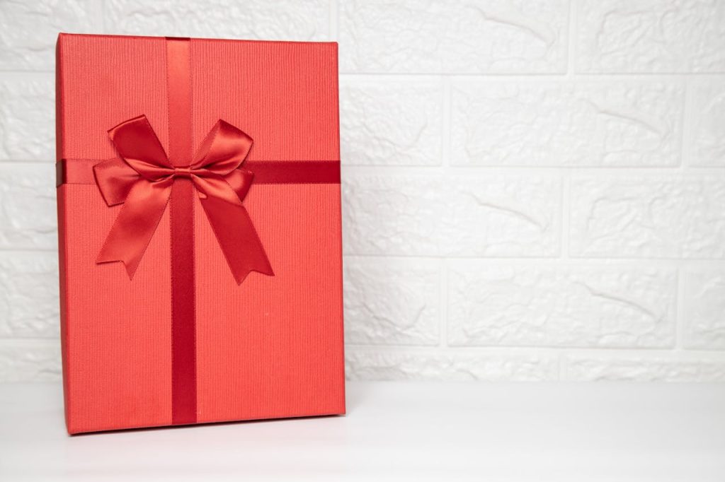 Elegant red gift box with a satin ribbon against a white textured background for celebrations.